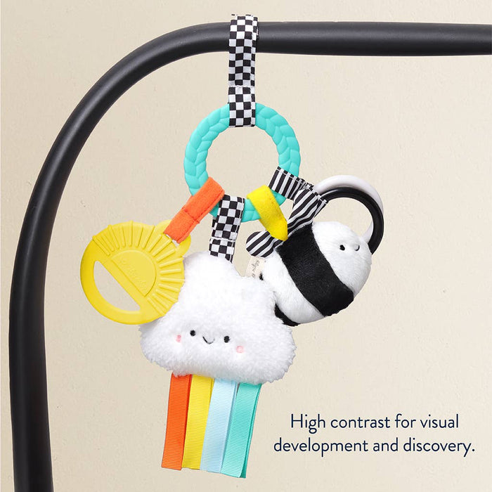 Colorful baby toy with cloud design hanging from a crib bar on a beige background.