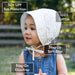 Child wearing a white eyelet sun hat with text highlighting features like SPF, cotton content, soft brim, and chinstrap.