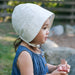 Child wearing a white bonnet and blue dress, holding a pink object outdoors.