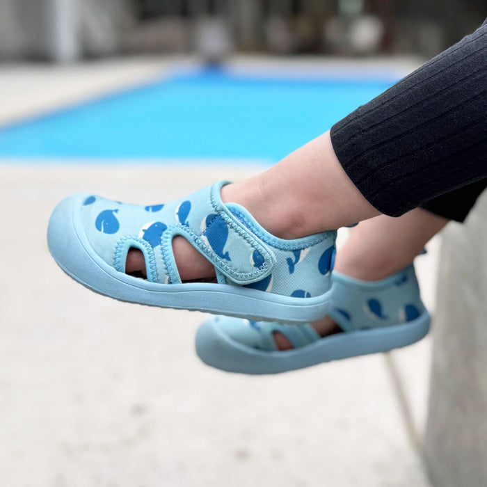 Child's foot wearing a blue sandal with paw prints on a poolside background