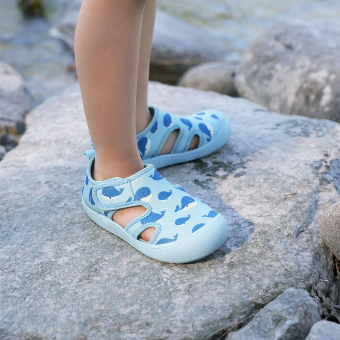 Children's feet wearing light blue sandals with whale pattern on rocky surface