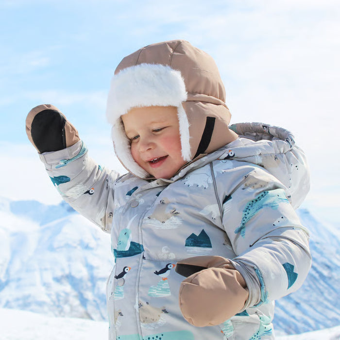 Child in a snowsuit with animal patterns standing in the snow.
