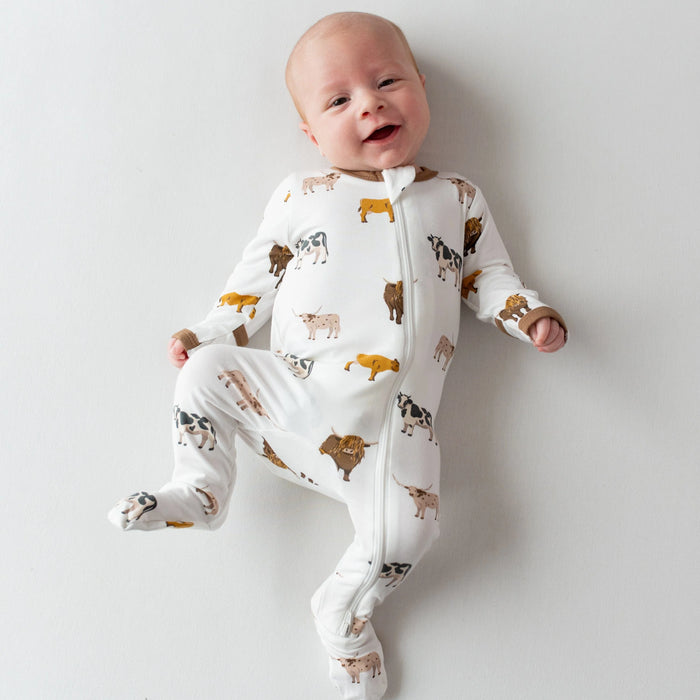Baby wearing a white onesie with animal prints on a plain background
