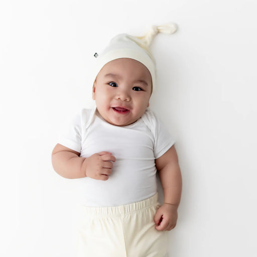 Baby wearing a white outfit with a matching hat on a light background