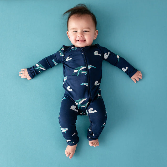 Baby wearing a navy blue onesie with humpback whale patterns on a blue background