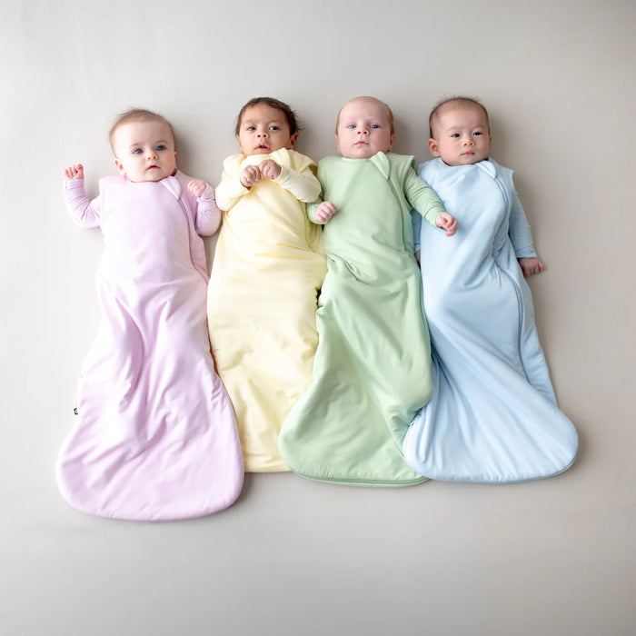 Four babies wrapped in pastel-colored swaddles on a neutral background