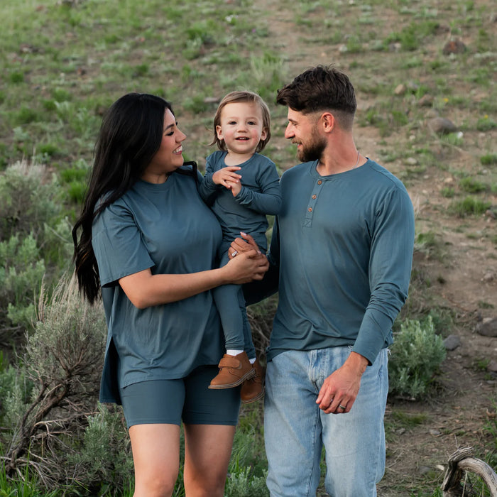 Family of three in matching teal outfits standing in a natural setting.