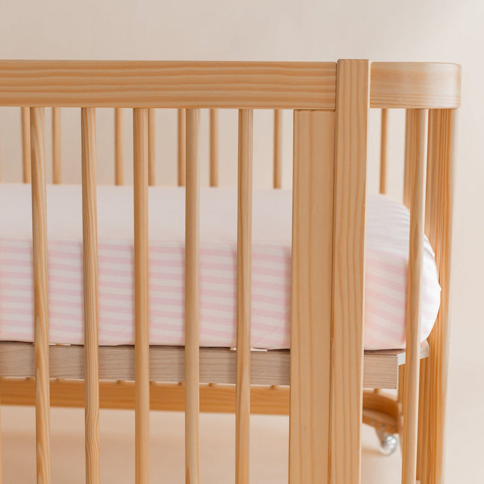 Wooden crib with pink striped sheet against a neutral wall