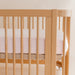 Wooden crib with pink striped sheet against a neutral wall