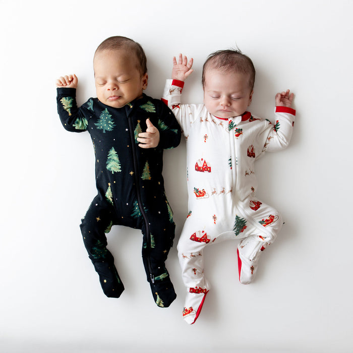 Two babies wearing kyte Christmas-themed onesies on a white background