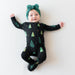 Baby wearing a black kyte onesie with green tree patterns and a matching headband on a white background