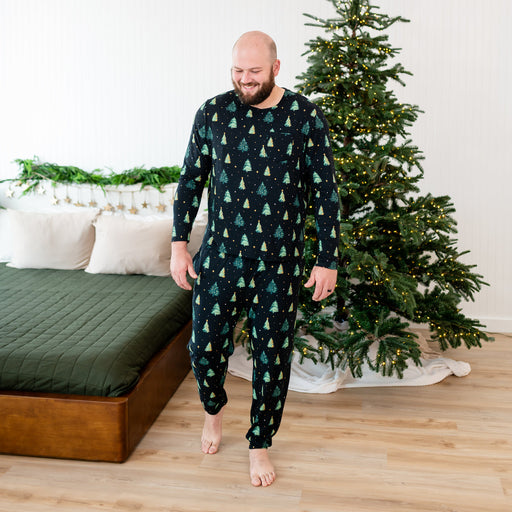 Man wearing a festive matching shirt and pants in a bedroom with a decorated Christmas tree.