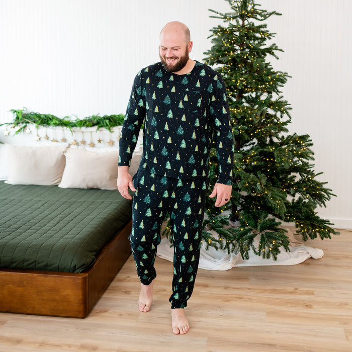 Man wearing a festive matching shirt and pants in a bedroom with a decorated Christmas tree.
