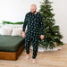 Man wearing a festive matching shirt and pants in a bedroom with a decorated Christmas tree.
