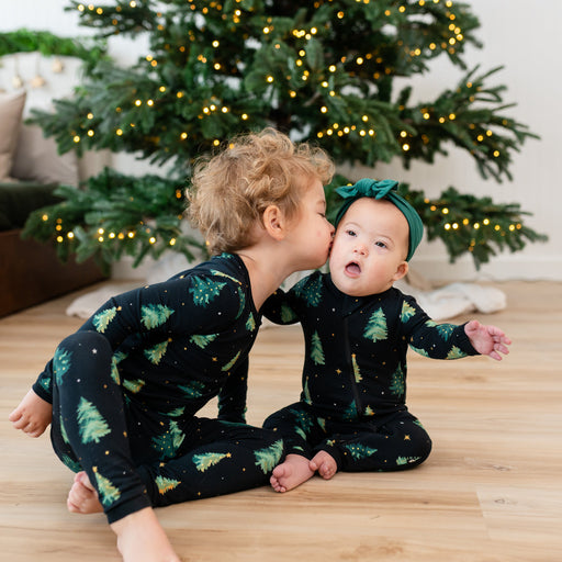Two children in matching kyte pajamas with a Christmas tree in the background