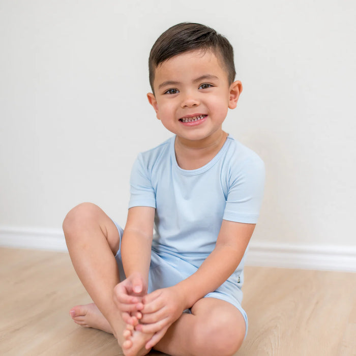 Child wearing light blue pajamas sitting on a bed.