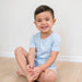 Child wearing light blue pajamas sitting on a bed.
