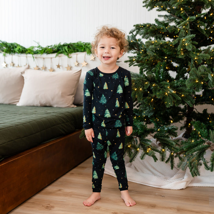 Child wearing Kyte Christmas-themed pajamas standing in front of a decorated Christmas tree.