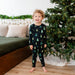 Child wearing Kyte Christmas-themed pajamas standing in front of a decorated Christmas tree.