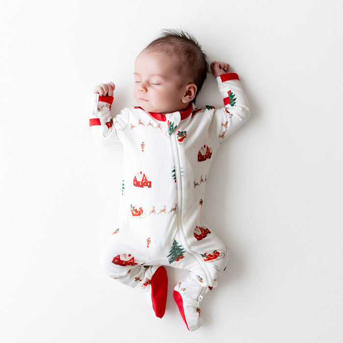 Newborn baby wearing a white kyte onesie with red and green patterns on a white background