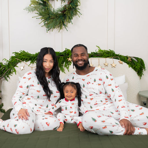 Family of three wearing matching kyte Christmas pajamas sitting on a couch with holiday decorations.
