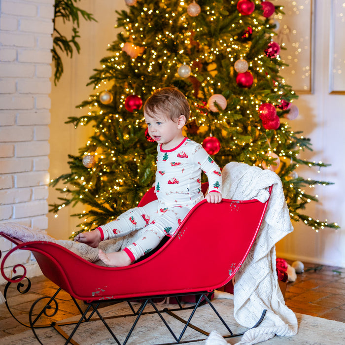Child in kyte pajamas sitting in a red sleigh in front of a decorated Christmas tree.