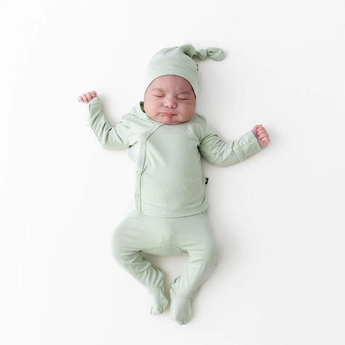 Sleepy newborn baby in a matching green outfit and hat lying on a white background