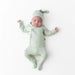 Sleepy newborn baby in a matching green outfit and hat lying on a white background