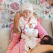 Baby in pink and white outfit being held by a caregiver with floral rug in the background