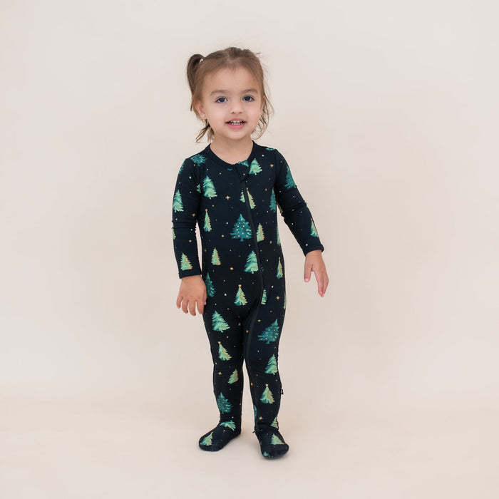 Child wearing a black kyte onesie with green tree pattern on a beige background