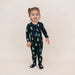 Child wearing a black kyte onesie with green tree pattern on a beige background