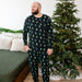Man wearing a black Christmas tree pattern kyte pajama set standing in front of a decorated Christmas tree.