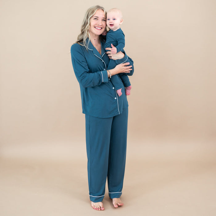 Woman in teal pajamas holding a baby against a beige background