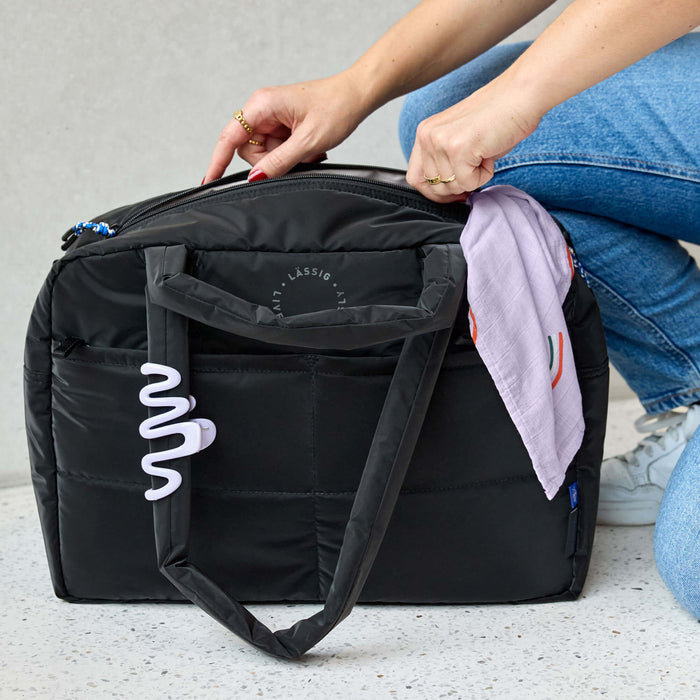 Person packing a black diaper bag with a colorful blanket inside, on a light gray surface.