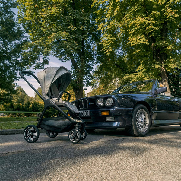 Black stroller next to a black BMW car on a tree-lined street