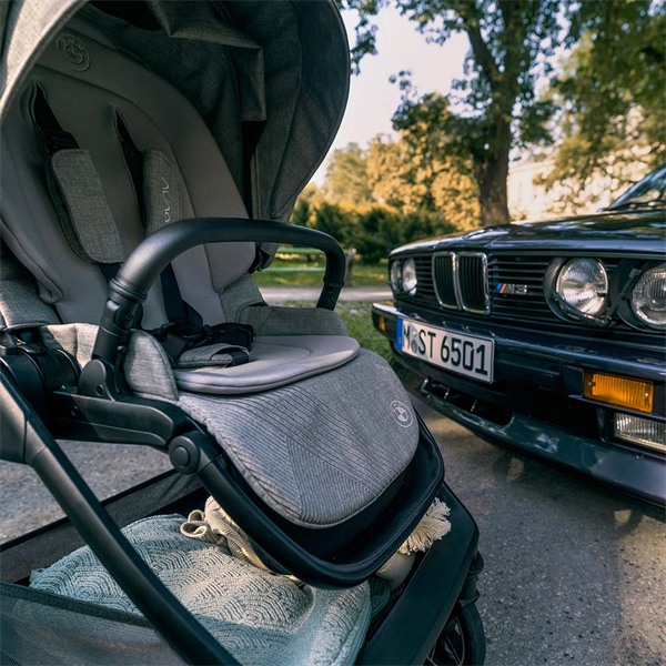 Gray baby stroller with a car in the background on a road.