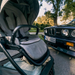 Gray baby stroller with a car in the background on a road.