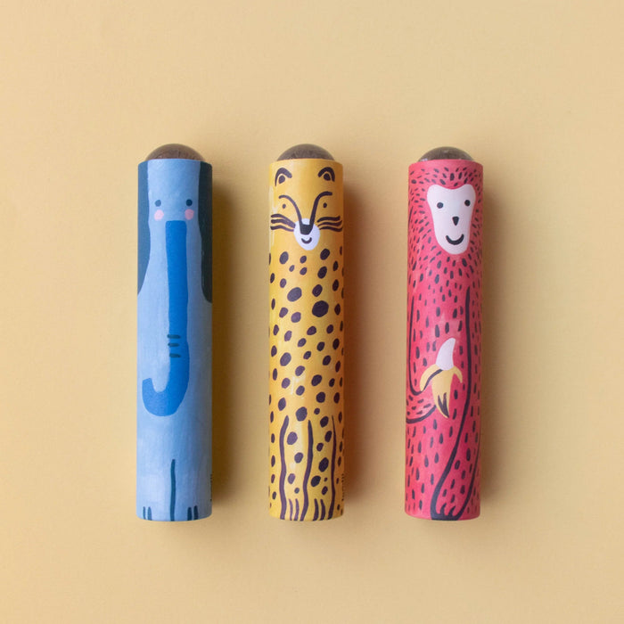 Three animal-shaped kaleidoscope toys on a warm beige background. The left one is blue with a stylized elephant design, the middle one is yellow with a cheetah design, and the right one is red with a monkey design.
