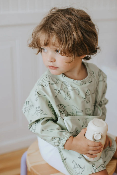 Child wearing a green animal-patterned poncho holding a white cup.
