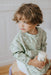 Child wearing a green animal-patterned poncho holding a white cup.