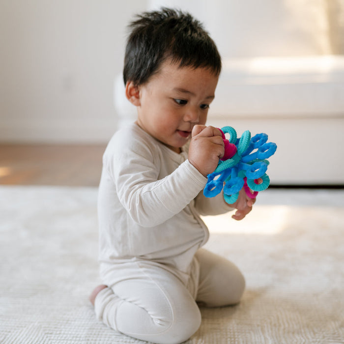 Baby sitting on a bed holding a colourful mobi toy