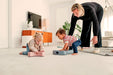 Woman and two children playing with my first toys on a carpeted floor in a living room.