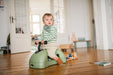 Child riding a green toy horse indoors on a wooden floor.