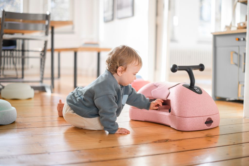 Child playing with a pink my first ride on on a wooden floor