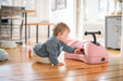 Child playing with a pink my first ride on on a wooden floor