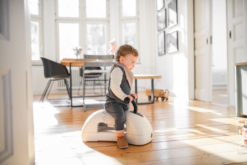 Child sitting on a white stool in a bright room with large windows.