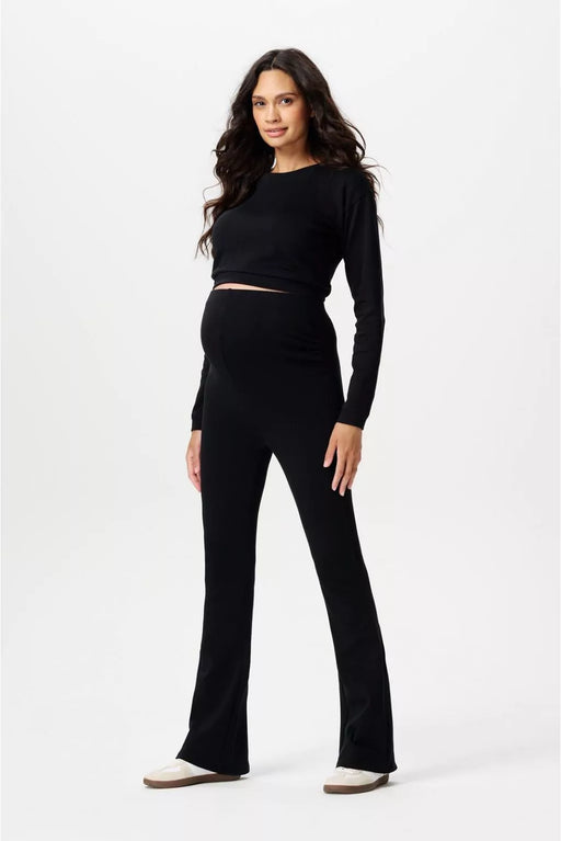 Woman wearing a black long-sleeve top and black flared maternity pants on a white background