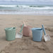 Colorful buckets and shovels on a sandy beach with ocean waves in the background