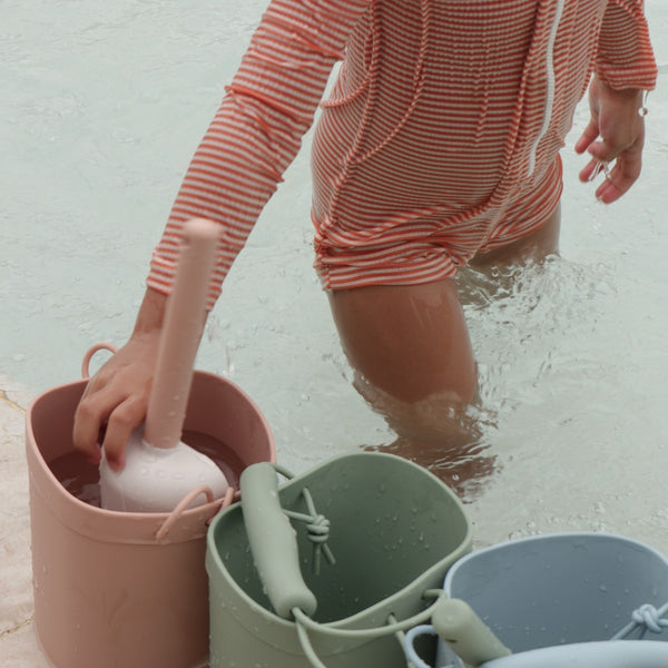 Child in striped swimsuit playing with buckets in water