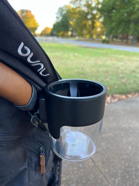 Black cup holder attached to a stroller with a park background